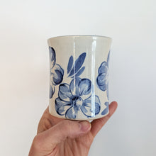 Load image into Gallery viewer, Hand holding a ceramic mug with blue floral patterns on a plain background