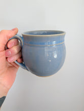 Load image into Gallery viewer, Hand holding a blue ceramic mug. 