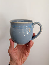 Load image into Gallery viewer, Hand holding a blue mug wheel thrown by Christi Becker pottery 